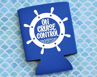 May include: A blue can cooler with a white ship's wheel design and the words "ON CRUISE CONTROL". The background is a light blue and white scale pattern.