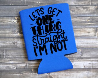 May include: A blue drinks can cooler with black text. The text says "LET'S GET ONE THING STRAIGHT I'M NOT". The cooler is made of a neoprene-like material. The background is a wooden surface.
