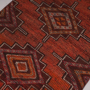 May include: A red, orange, and brown patterned rug with a geometric design. The rug has a diamond pattern with smaller diamonds inside.