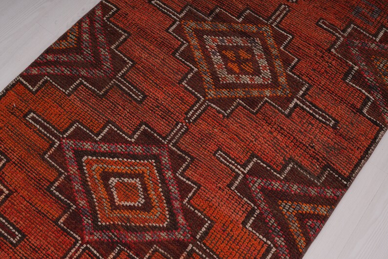 May include: A red, orange, and brown patterned rug with a geometric design. The rug has a diamond pattern with smaller diamonds inside.