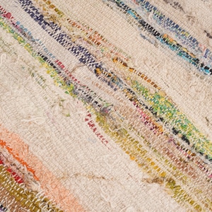 May include: A woven rug featuring a textured, off-white base with diagonal stripes of multicolored fabric strips. The textile displays a variety of vibrant hues including orange, blue, green, yellow, and red, integrated into the weave.