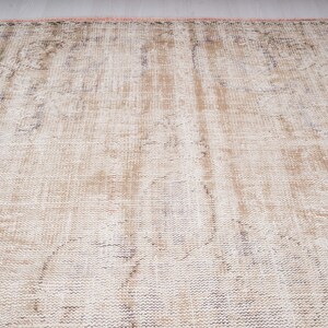 Op de afbeelding: Een vintage-stijl tapijt met een vervaagd, verweerd patroon in beige en witte tinten. Het tapijt heeft een geweven textuur en een licht versleten uiterlijk.