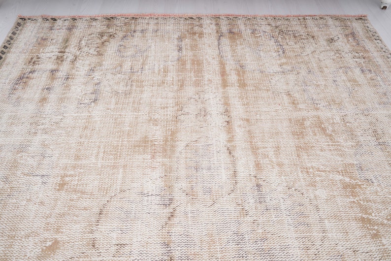 Op de afbeelding: Een vintage-stijl tapijt met een vervaagd, verweerd patroon in beige en witte tinten. Het tapijt heeft een geweven textuur en een licht versleten uiterlijk.