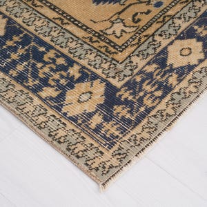 May include: A beige rug with a blue and cream patterned border. The rug has a traditional design with intricate details.