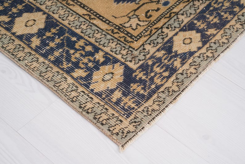 May include: A beige rug with a blue and cream patterned border. The rug has a traditional design with intricate details.