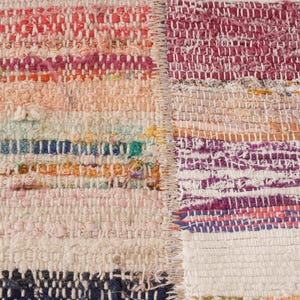 May include: A woven rag rug featuring a patchwork design with two distinct sections joined by a vertical seam. The fabric strips display a multicolored palette including shades of pink, orange, blue, white, and purple in a textured weave.