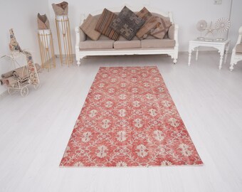 May include: A rectangular, red and cream-colored rug with an intricate floral pattern. The rug is the focal point of a room with a white floor, a beige sofa, and decorative items.