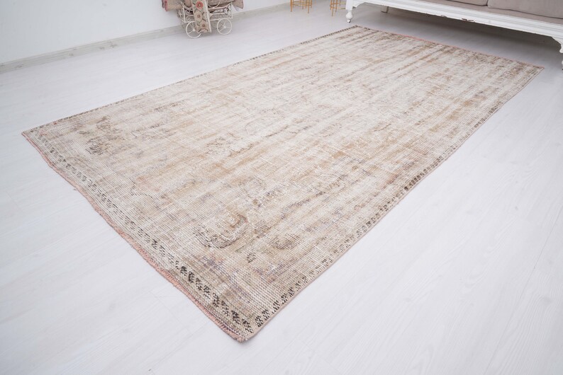 Op de afbeelding: Een licht beige vloerkleed met een vervaagd bloemenpatroon en een roze rand. Het kleed heeft een verweerde, vintage uitstraling.