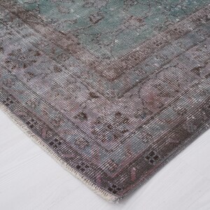 May include: Close-up of the edge of a vintage rug with a faded, multi-colored pattern. The rug has a frayed, hand-woven edge and a soft, worn texture.