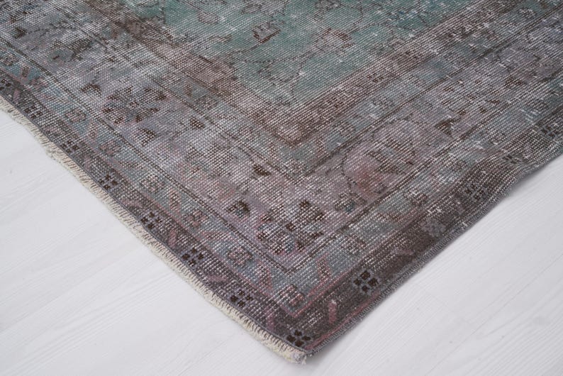 May include: Close-up of the edge of a vintage rug with a faded, multi-colored pattern. The rug has a frayed, hand-woven edge and a soft, worn texture.