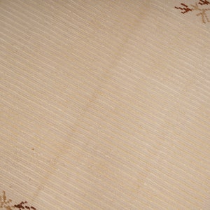 Pu&ograve; includere: Primo piano di un tessuto beige con un sottile motivo intrecciato. Il tessuto ha una delicata lucentezza quasi iridescente. Il tessuto &egrave; decorato con un semplice motivo a fiocco di neve marrone negli angoli.