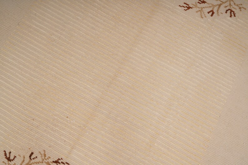Pu&ograve; includere: Primo piano di un tessuto beige con un sottile motivo intrecciato. Il tessuto ha una delicata lucentezza quasi iridescente. Il tessuto &egrave; decorato con un semplice motivo a fiocco di neve marrone negli angoli.