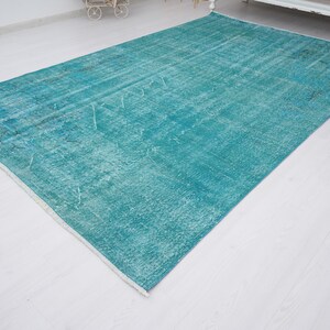 May include: A teal blue rug with a faded, distressed pattern. The rug has a white border and is laid out on a white floor.