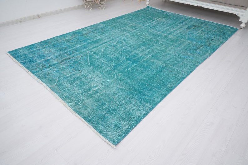 May include: A teal blue rug with a faded, distressed pattern. The rug has a white border and is laid out on a white floor.