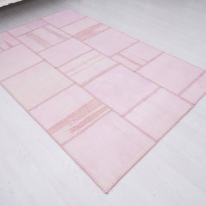 May include: A pink patchwork rug made of various sized squares of fabric sewn together. The rug has a light pink color and a slightly distressed look.