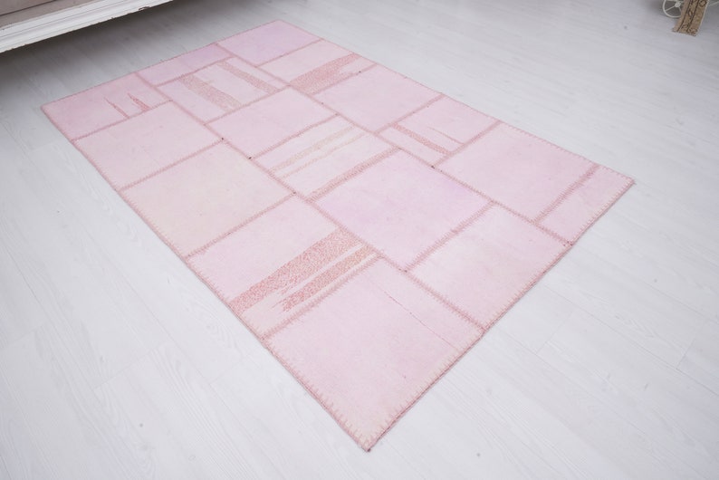May include: A pink patchwork rug made of various sized squares of fabric sewn together. The rug has a light pink color and a slightly distressed look.