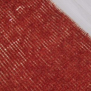 Puede incluir: Una alfombra de color rojo intenso con textura que presenta una superficie de pelo denso y anudado con sutiles variaciones verticales en la intensidad del color y un borde cosido reforzado de color claro a lo largo del borde diagonal.