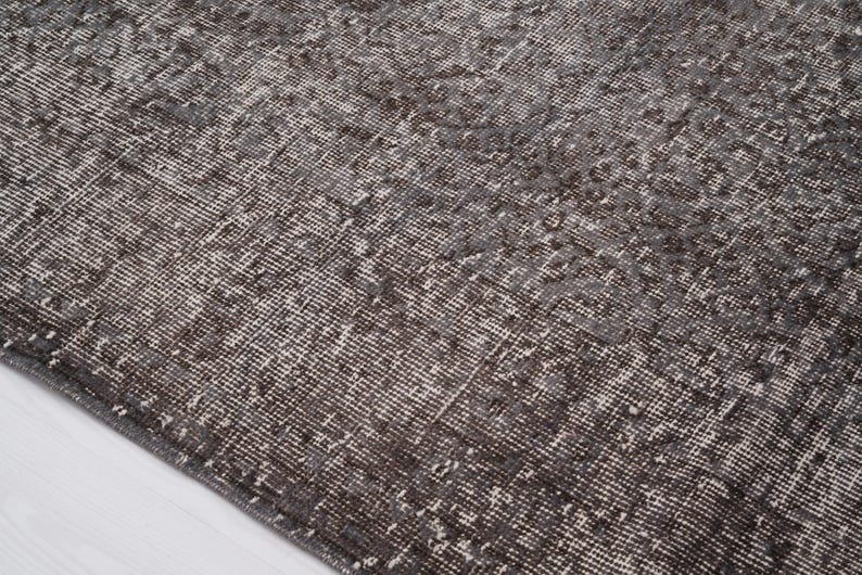 May include: A close-up of a dark gray rug with a subtle pattern. The rug has a distressed, vintage look and is made of a soft, woven material.