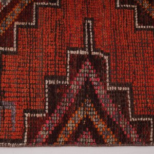 May include: Close-up of a red, orange, and brown patterned rug with a fringe border. The rug has a geometric design with a dark brown center.