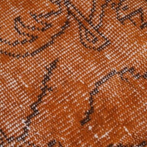 Puede incluir: Un tejido con un color base naranja quemado vibrante que presenta un patr&oacute;n repetitivo de motivos lineales oscuros y dentados en marr&oacute;n, junto con peque&ntilde;as motas blancas distribuidas por toda la superficie, creando un aspecto texturizado.