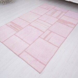 May include: A pink patchwork rug with a variety of squares and rectangles sewn together. The rug has a light pink color and a subtle sheen.