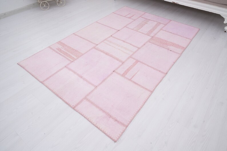 May include: A pink patchwork rug with a variety of squares and rectangles sewn together. The rug has a light pink color and a subtle sheen.
