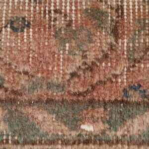 May include: Close-up of a section of a vintage rug with a distressed, faded appearance. The rug features a mix of colors, including muted reds, greens, and browns, with a cream-colored border and accents. The design has a traditional, floral pattern.