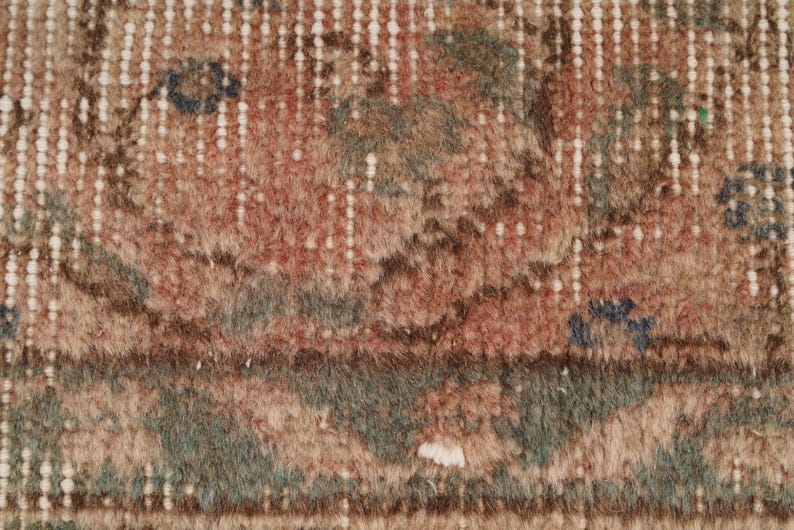 May include: Close-up of a section of a vintage rug with a distressed, faded appearance. The rug features a mix of colors, including muted reds, greens, and browns, with a cream-colored border and accents. The design has a traditional, floral pattern.