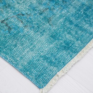 May include: A teal blue rug with a white fringe. The rug has a woven texture and a faded, vintage look.