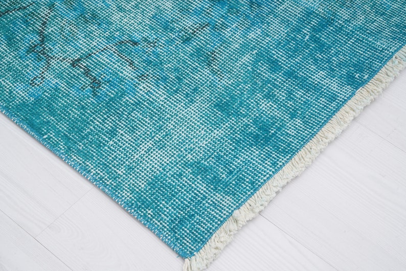 May include: A teal blue rug with a white fringe. The rug has a woven texture and a faded, vintage look.