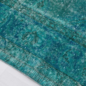 May include: Close-up of a teal blue and white vintage rug with a distressed, faded look. The rug has a woven texture and a subtle pattern.