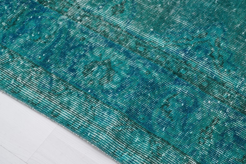 May include: Close-up of a teal blue and white vintage rug with a distressed, faded look. The rug has a woven texture and a subtle pattern.