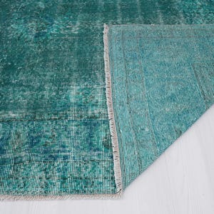 May include: Close-up of a teal blue rug with a fringe edge. The rug is folded in half, showing the underside of the rug.