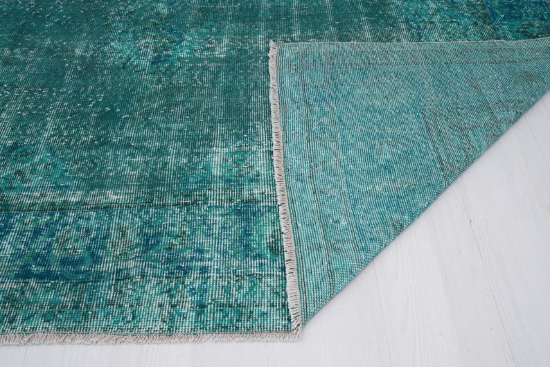 May include: Close-up of a teal blue rug with a fringe edge. The rug is folded in half, showing the underside of the rug.
