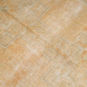 May include: Close-up of a vintage rug with a geometric pattern. The rug features a warm color palette of beige, orange, and cream. The design includes repeating diamond and zigzag shapes, creating a textured appearance.