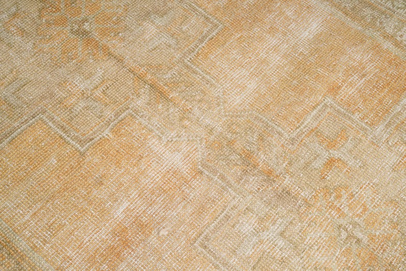 May include: Close-up of a vintage rug with a geometric pattern. The rug features a warm color palette of beige, orange, and cream. The design includes repeating diamond and zigzag shapes, creating a textured appearance.