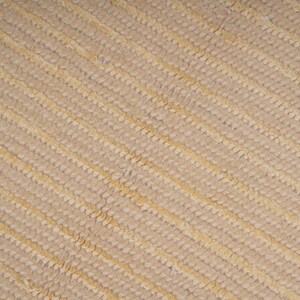 Pu&ograve; includere: Primo piano di un tessuto beige testurizzato con un motivo diagonale di linee in rilievo.