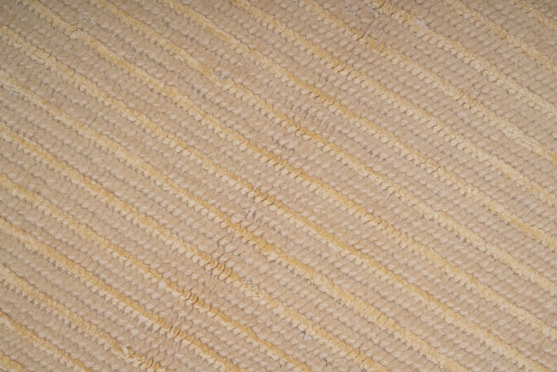 Pu&ograve; includere: Primo piano di un tessuto beige testurizzato con un motivo diagonale di linee in rilievo.