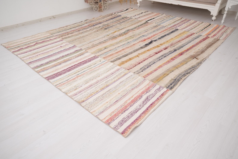 May include: A large rectangular area rug featuring a patchwork design composed of multiple strips of fabric. The rug displays a variety of muted colors including beige, cream, soft pink, muted yellow, light blue, and grey in a striped pattern.