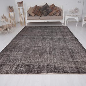 May include: A dark gray distressed rug with a subtle pattern. The rug is laid out on a white floor in a room with white walls and furniture.