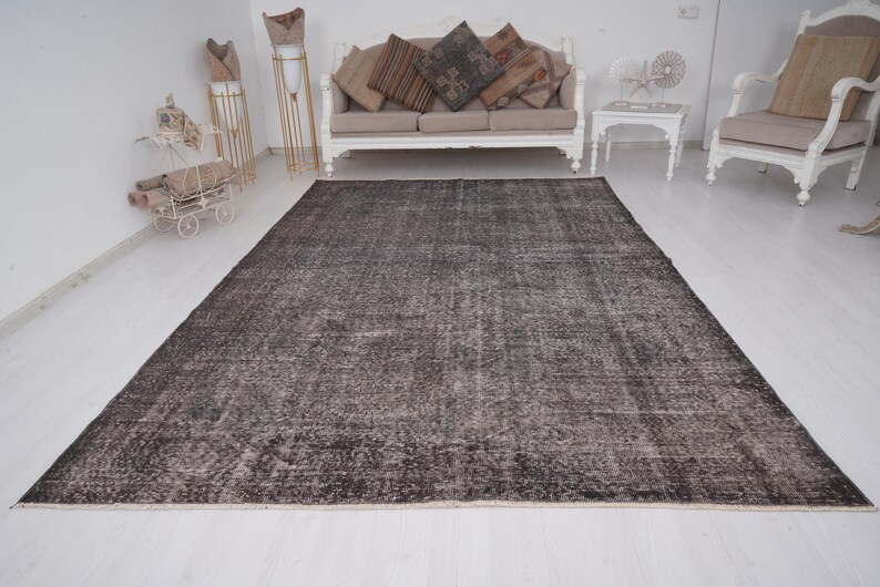 May include: A dark gray distressed rug with a subtle pattern. The rug is laid out on a white floor in a room with white walls and furniture.