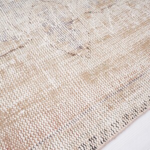 Op de afbeelding: Close-up van een geweven beige en wit tapijt met een textuur. Het tapijt heeft een subtiel patroon van licht en donker beige strepen.