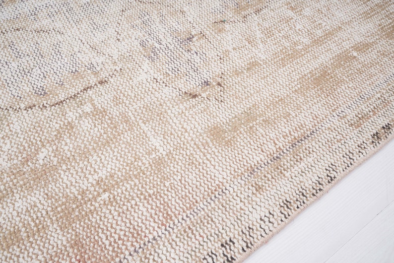 Op de afbeelding: Close-up van een geweven beige en wit tapijt met een textuur. Het tapijt heeft een subtiel patroon van licht en donker beige strepen.