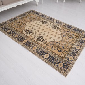 May include: A beige and blue patterned rug with a central diamond shape. The rug has a traditional design with intricate details.