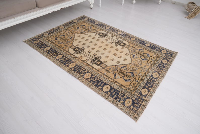 May include: A beige and blue patterned rug with a central diamond shape. The rug has a traditional design with intricate details.