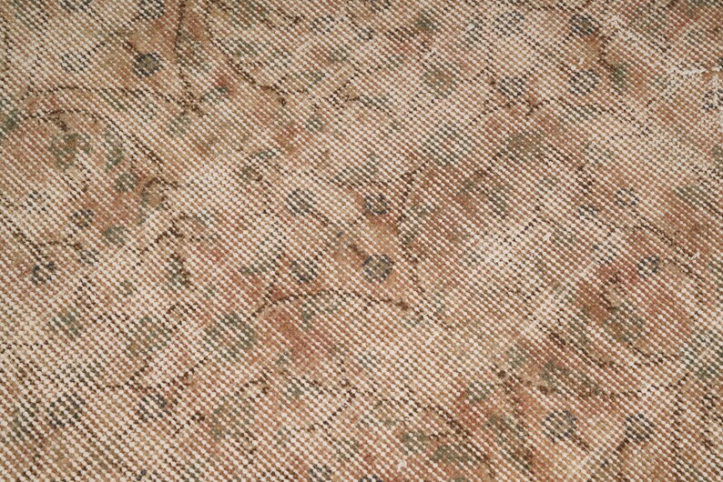 May include: Close-up of a vintage rug with a detailed, woven pattern. The rug features a beige background with intricate designs in shades of brown, green, and rust. The texture appears soft and well-worn.