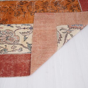 Puede incluir: Una alfombra rectangular con un dise&ntilde;o de patchwork que combina secciones de color naranja quemado, crema y rojo oscuro. La secci&oacute;n crema muestra intrincados patrones florales en tonos apagados, mientras que la naranja tiene motivos florales oscuros.