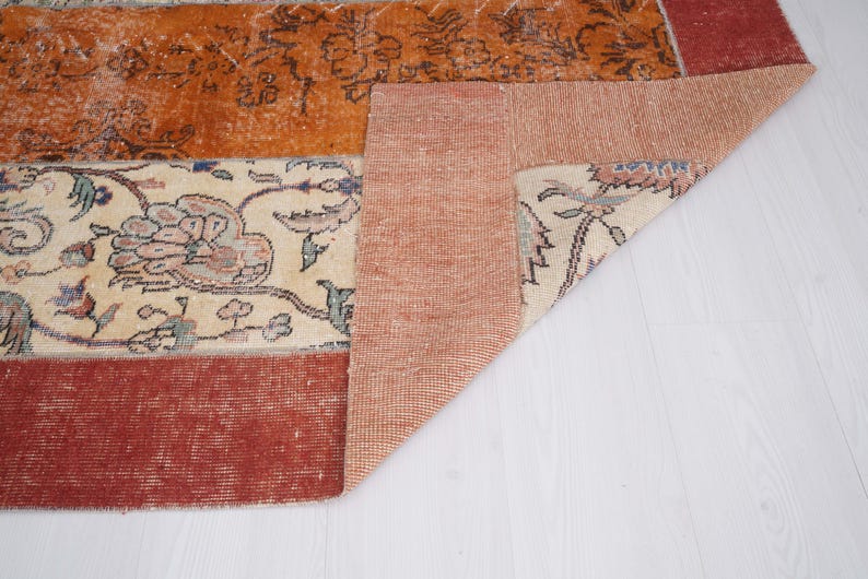 Puede incluir: Una alfombra rectangular con un dise&ntilde;o de patchwork que combina secciones de color naranja quemado, crema y rojo oscuro. La secci&oacute;n crema muestra intrincados patrones florales en tonos apagados, mientras que la naranja tiene motivos florales oscuros.