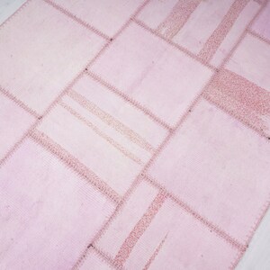 May include: A pink patchwork rug with a geometric pattern. The rug is made of different pieces of fabric sewn together.