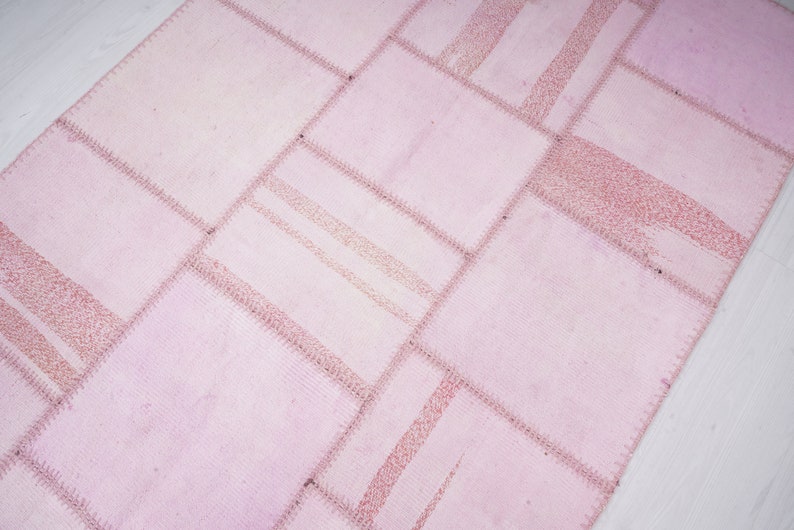 May include: A pink patchwork rug with a geometric pattern. The rug is made of different pieces of fabric sewn together.